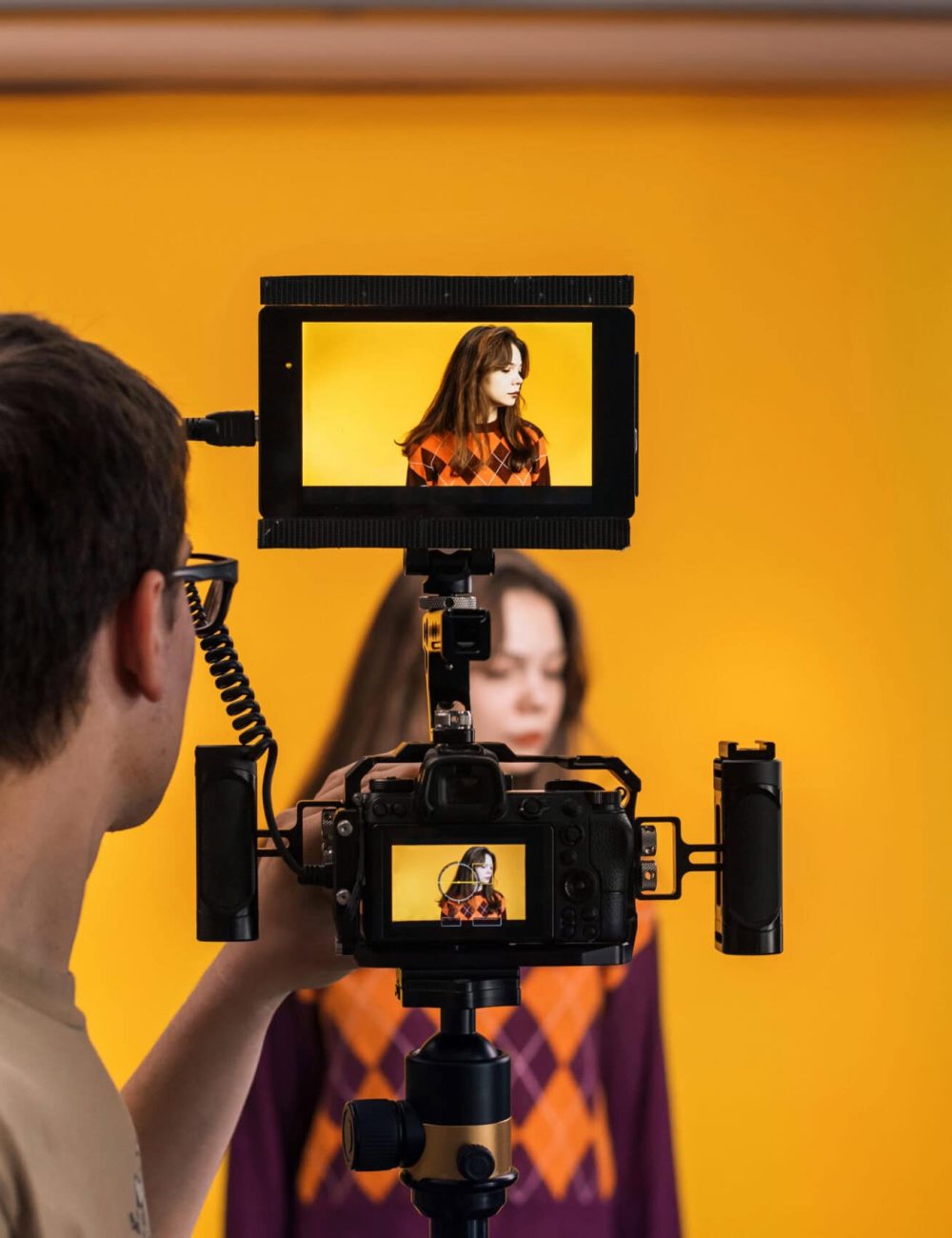View of a professional photographer shooting a young woman using a camera with external display, yellow background